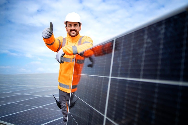 A professional worker standing by a solar panel and holding thumbs up in Atlanta, GA 